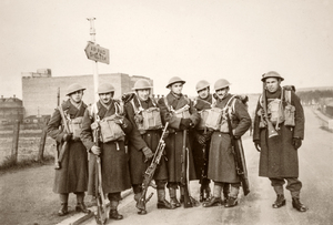 Polscy oficerowie w pełnym rynsztunku, ubrani w płaszcze sukienne z oporządzeniem brytyjskim typu P-37, na głowach mają hełmy brytyjskie Mk II, wyposażeni są w karabiny Lee-Enfield oraz RKM typu Bren. Zdjęcie wykonane w Szkocji ok. 1941 r. Drugi z lewej z ppor. Władysław Jaksan. Na zdjęciu tablica informacyjna z napisem: „AIR RAID SHELTER” (schron przeciwlotniczy).