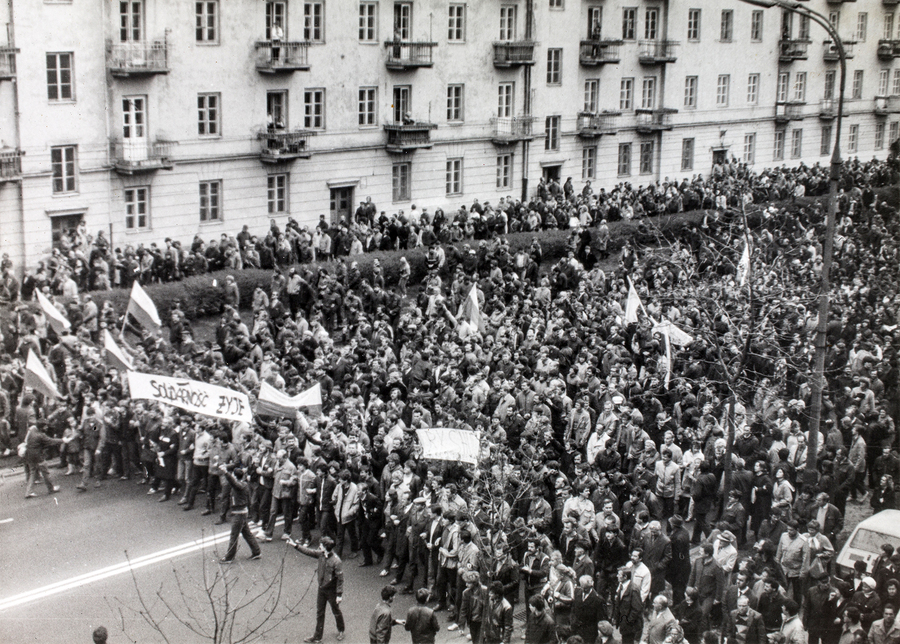 Zdjęcie 014. Sympatycy i działacze NSZZ „Solidarność” idą w pochodzie ulicą Słowackiego od strony Placu Komuny Paryskiej w pobliżu kamienicy przy ul. Słowackiego 38 w Warszawie 1 maja 1985 r. Na zdjęciu widoczne są transparenty z napisami: „SOLIDARNOŚĆ ŻYJE”, „RKS HUTA im. ks. J. Popiełuszki”.